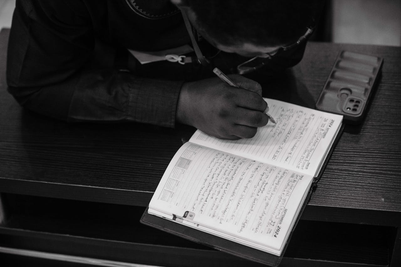 Black and white photo of a person writing in a journal, capturing focus and devotion.